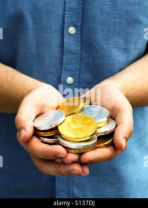 Une paire de mains tenant une poignée d'or et d'argent des pièces de chocolat. Banque D'Images