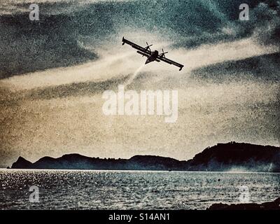 Lutte contre l'incendie dans l'avion amphibie ciel rempli de fumée, après avoir recueilli l'eau de mer pour lutter contre les feux de forêt à proximité. Banque D'Images