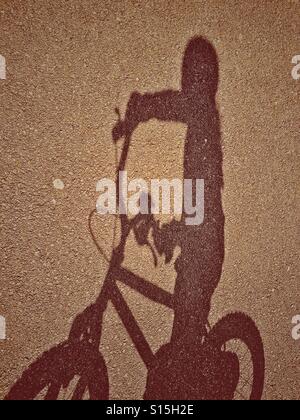 L'ombre d'une fille de 4 ans sur certains Tarmac comme elle chevauche son vélo en plein air au parc de la pièce. Une image pour illustrer l'enfance. Crédits photos - © COLIN HOSKINS. Banque D'Images