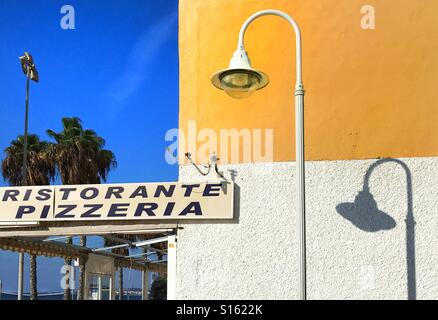 Ristorante Pizzeria affiche à l'extérieur restaurant en terrasse extérieure couverte sur coin salon sous un bleu ciel sans nuages à côté de mur extérieur peint en jaune clair et blanc brillant Banque D'Images