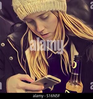 Teenage girl looking at son iPhone tout en tenant une bouteille de bière. Banque D'Images