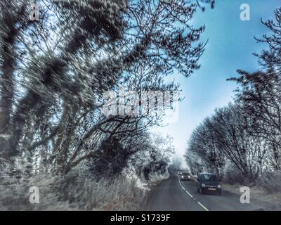 Vue du conducteur à travers le pare-brise de la route en hiver. Givre lourd, au verglas et voitures approche avec projecteurs. Tôt le matin. Banque D'Images