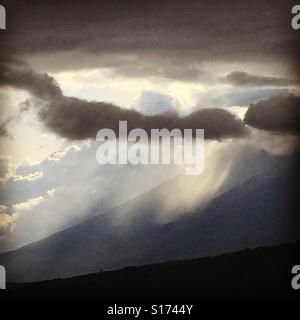 Coucher du soleil les faisceaux lumineux à travers la pluie qui tombe sur les volcans près de Antigua, Guatemala, Amérique Centrale Banque D'Images