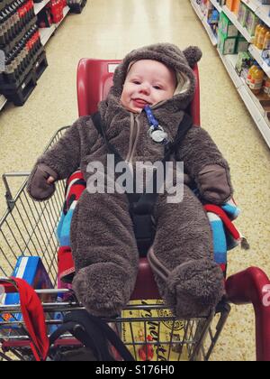 Trois mois bébé garçon vêtu d'un costume d'ours. Assis dans un chariot de supermarché Banque D'Images