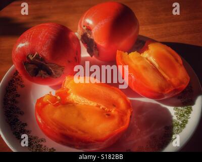 Trois kakis sur une plaque, une coupe ouverte et prête à manger. Banque D'Images