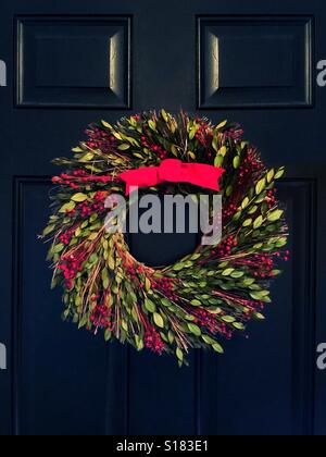 Une couronne de Noël avec un arc rouge sur une porte noire Banque D'Images