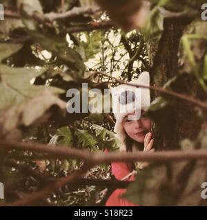 Girl wearing hat ours se cacher derrière arbre, UK Banque D'Images