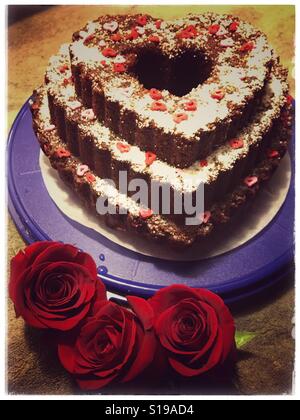 Gâteau au chocolat en forme de coeur avec des roses rouges en premier plan Banque D'Images