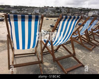 Une ligne de bleu et blanc à rayures transats avec vue sur les bateaux de pêche sur la plage à St Ives en Cornouailles, dans le sud de l'Angleterre Banque D'Images