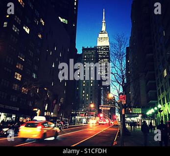 Trafic sur 34th Street, près de l'Empire State building éclairé en lumière blanche au crépuscule, NYC, USA Banque D'Images