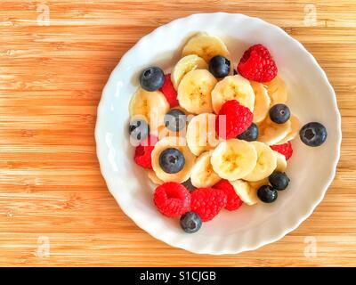 Bol de yogourt garni de banane fraîche, bleuets et framboises sur un conseil de bambou with copy space Banque D'Images