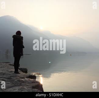 Une femme se tient sur le bord d'un lac magnifique au lever du soleil. Banque D'Images