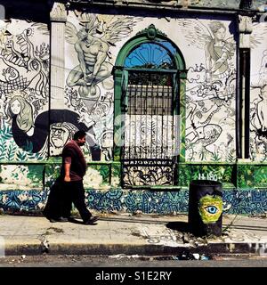 Un homme marche devant une maison en ruine avec des éléments de l'architecture coloniale espagnole, peint par un artiste local, dans le centre de San Salvador, El Salvador, 12 novembre 2016. Banque D'Images