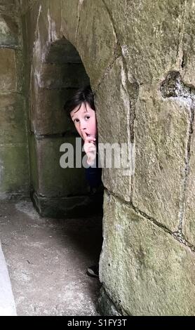 Un jeune garçon joue à cache-cache dans une ancienne arche en pierre. Banque D'Images