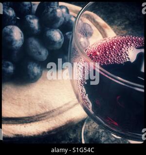 Un verre de vin rouge avec quelques 'Autumn Royal' table [manger] raisins sur une planche de bois. Banque D'Images