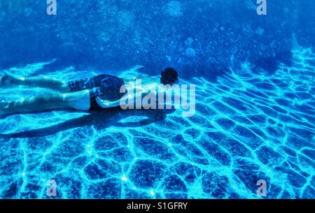 Teenage boy swimming underwater in d'une piscine extérieure. Banque D'Images