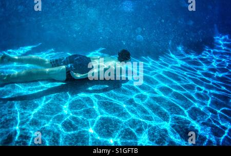 Teenage boy swimming underwater in d'une piscine extérieure. Banque D'Images