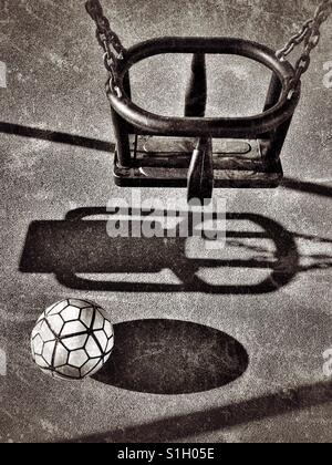 Ombre d'un swing et le football dans une aire de jeux pour enfants. Personne n'est présent. Où sont les enfants ? Une image avec de multiples usages. Photo © COLIN HOSKINS. Banque D'Images