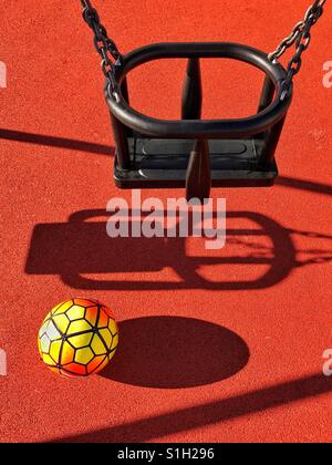 Une famille se trouve sous football un seul swing dans une aire de jeux pour enfants. C'est un bel après-midi d'été il y a des ombres. Où sont les enfants ? Photo © COLIN HOSKINS. Banque D'Images