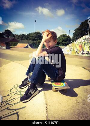 Un garçon de 10 ans aux cheveux rouges refroidissement sur son skateboard à l'Eaton Skatepark à Norwich, Royaume-Uni Banque D'Images