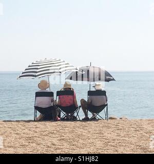 Un groupe de personnes âgées s'asseoir sur des chaises longues sous des parasols sur l'un des jours les plus chauds de l'année à West Bay, Dorset Banque D'Images