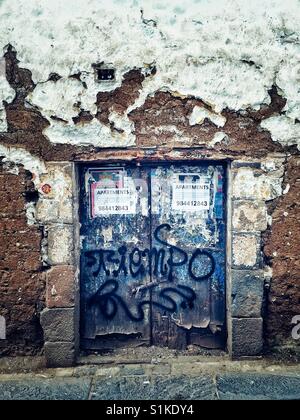 Vieille porte bleue avec peint à la bombe des graffitis et plâtré avec des annonces dans le mur en stuc blanc hirsute sur la rue de Cusco, Pérou Banque D'Images