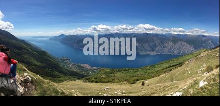 Le lac de Garde, Italie - Mai 2017 : vue panoramique depuis le Monte Baldo à jusqu'à Malcesine avec un visiteur assis sur un rocher Banque D'Images