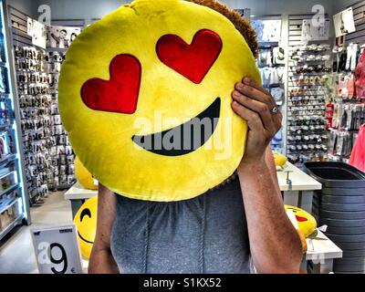 Femme tenant un je t'aime coussin d'émoticônes sur son visage dans un magasin Banque D'Images