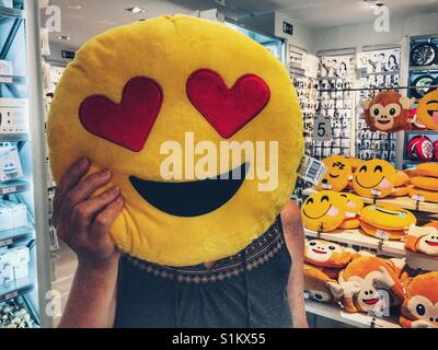 Femme tenant un je t'aime coussin d'émoticônes sur son visage dans un magasin Banque D'Images