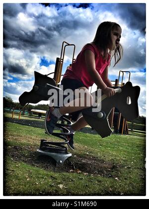 5 ans, fille, sur un cheval à bascule au parc. Banque D'Images