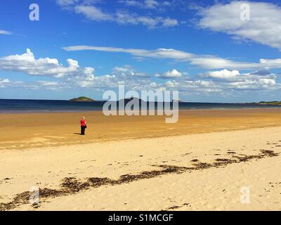 Une femme marche sur une large plage. Banque D'Images