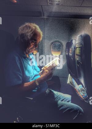 Senior man reading a book dans un avion dans la nuit, l'attente pour le décollage Banque D'Images