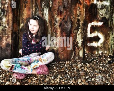 5 ans, assis à côté de la digue, Ferry Bawdsey, Suffolk, Angleterre. Banque D'Images