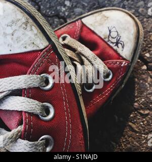 Close up detail d'une vieille paire de chaussures de toile rouge sur une surface d'asphalte Banque D'Images