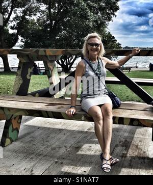 Femme assise sur une grande table de pique-nique dans un parc le long du secteur riverain de Toronto. Banque D'Images