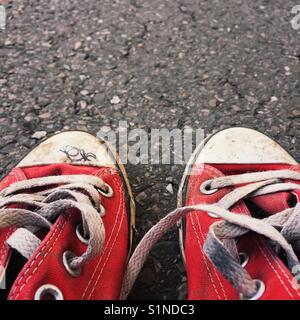 Close up detail d'une vieille paire de chaussures de toile rouge sur une surface d'asphalte Banque D'Images