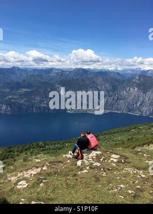 Un couple en vacances assis sur un rocher sur le Mont Baldo surplombant le lac de Garde, Italie Banque D'Images