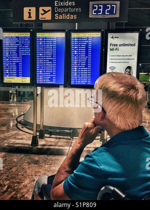 Hauts homme en fauteuil roulant la lecture de la carte de départ dans la nuit. El Altet aéroport, Alicante, Espagne. Banque D'Images