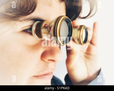 Femme millénaire regardant à travers une paire de lunettes d'opéra, jumelles à l'ancienne pour une utilisation au théâtre ou à l'opéra Banque D'Images