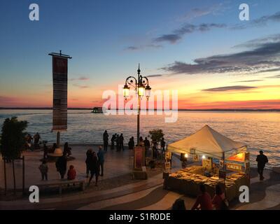 Via Sponchi, Lazise, Italie, côté lac ou le conseil à pied dans le port avec les piétons , les touristes et cafés sous ciel rouge orange jaune à l'automne sur Lago del Garda, sosie Rio de Janeiro Banque D'Images