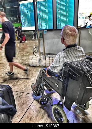 Hauts homme en fauteuil roulant à la recherche d'un vol au départ de l'aéroport d'El Altet, Alicante, Espagne Banque D'Images