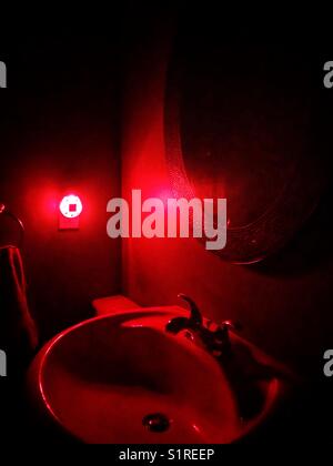 Lavabo de salle de bains éclairé par une veilleuse rouge Banque D'Images