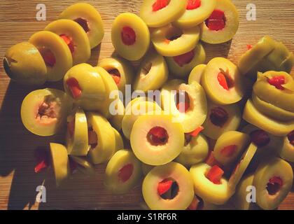 Tranches d'olives vertes fourrées de pimento sur une planche à découper en bois éclairée par le soleil de fin d'après-midi. Banque D'Images