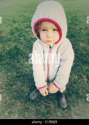 Fille de deux ans en manteau à capuche à l'extérieur avec expression de plaidoyer Banque D'Images