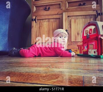 Bébé fille sur le ventre jouant avec jouet de ferme sur un plancher en bois Banque D'Images