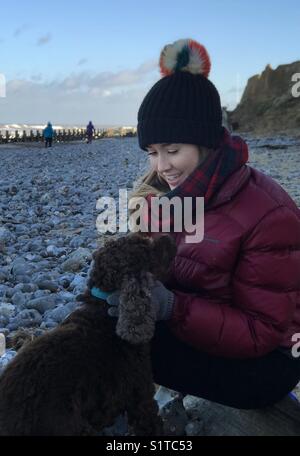 Jeune femme sur une plage de galets avec un épagneul cocker en hiver Banque D'Images