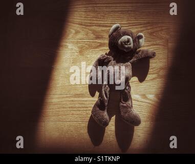 Ours en peluche brun vintage déposé dans un rayon de soleil sur un plancher en bois Banque D'Images