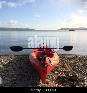 Un voyant rouge s'asseoir sur le kayak sur une plage avec une mer plate à l'arrière-plan Banque D'Images