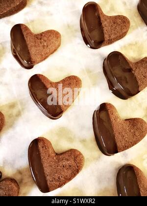 Boulangerie juste en forme de coeur chocolat cookies sont partiellement trempé dans du chocolat et sont placés sur une feuille de biscuit pour sécher. Banque D'Images