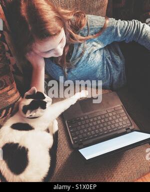 Jeune fille portant sur canapé à l'aide d'un ordinateur portable avec chat paw s'étendant sur près de bas à côté de son clavier Banque D'Images